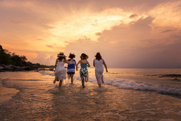Fototapeta premium Summer of Happy girls running together on sunset sea beach. Holiday concept. Cinema film tone with grain.