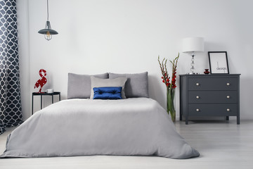 A monochromatic gray designer bedroom interior with a big bed and drawer cabinet and with...