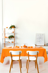 Poster on cabinet in white and orange dining room interior with wooden chairs at table. Real photo