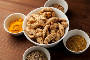Raw dry soya meat chunks in a white bowl on a wooden table with different species