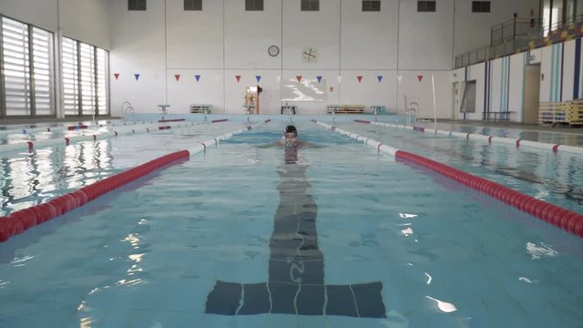 Swimmer In Pool Finishes Breaststroke Swim. Male swimmer exercising alone in a professional swimming pool. Steady shot