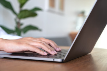 Closeup image of woman's hands using and typing on laptop keyboard on wooden table in office