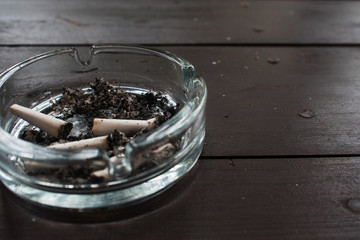 Glass ashtray with cigarette butts on wooden table