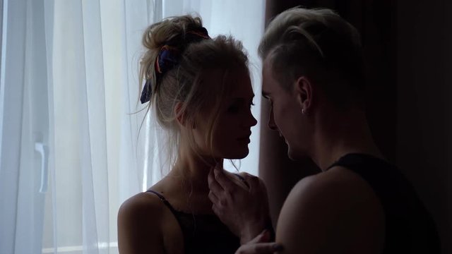 Silhouettes of young man and woman touching each other tender before a bright window in the room