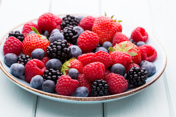 Fresh berry salad on blue dishes. Vintage wooden background.