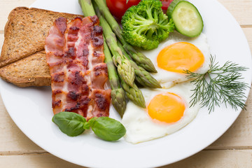Fried eggs with bacon on the wooden table.