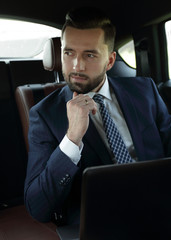 businessman with laptop sitting in a comfortable car