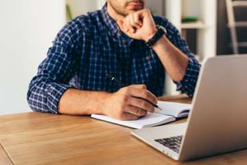 cropped shot of businessman with notebook taking part in webinar in office