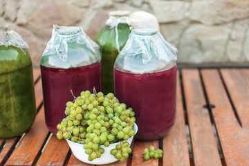 Close-up of a bunches of yellow ripe grapes from an organic garden. Wine bottle aback. Settled on the wooden table, stone wall background. The process of making home-made vine.