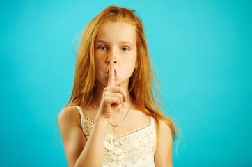 Red haired girl with strict look puts her finger to lips, demonstrates secret and confidentiality,...
