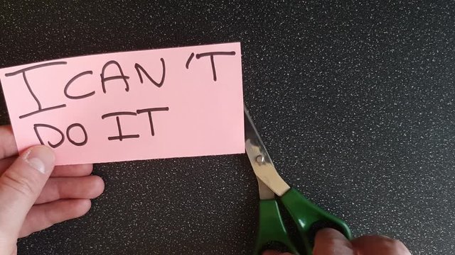 Man using scissors to remove the t from the word can't t leaving the positive motivational part. I can do it.