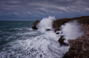 Dramatic nature background - big waves and dark rock in stormy sea, stormy weather. Dramatic scene. Contrasting colors.Beautiful natural landscape, seascape at Tyulenovo, Bulgaria. 