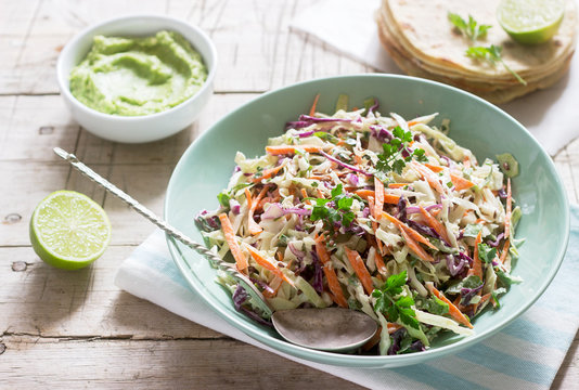 Coleslaw made from cabbage, carrots and various herbs, served with tortillas and guacamala on a wooden background.