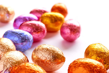 Many chocolate easter eggs wrapped in blue, purple, orange, pink and golden foil on a white background	
