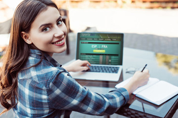 smiling beautiful girl using laptop with sportsbet page at table in street cafe