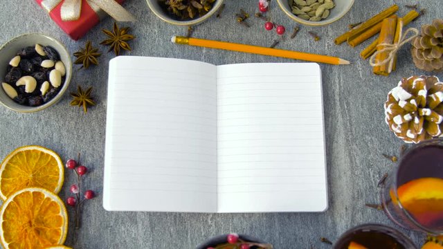 christmas and seasonal drinks concept - notebook with pencil, hot mulled wine and aromatic spices on grey background