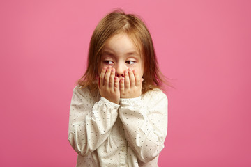 Child girl covered her mouth with hands and looks away with regret