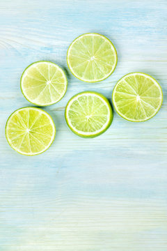 An overhead photo of many vibrant lime slices on a teal blue background with copy space