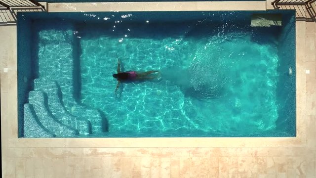Aerial view of young woman diving into swimming pool.