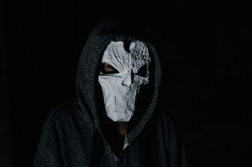 man in a hood and skull mask on a black background