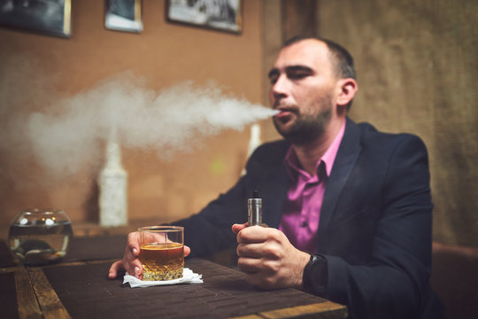 A man in a bar drinks whiskey and smokes a cigarette