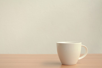 White coffee cup on wood table with copy space on white wall background.