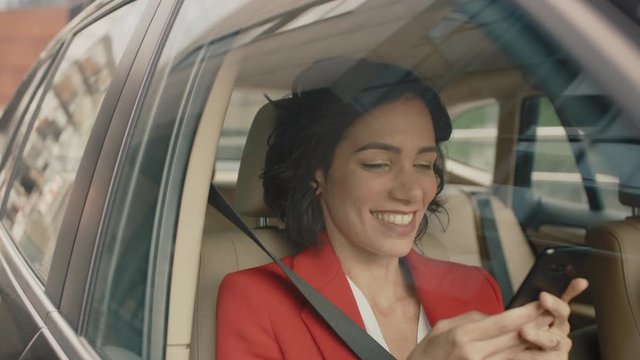 Beautiful Woman Traveling in a Car, Sitting on a Passenger Seat Uses Smartphone, types Message, Browses Through Internet. Camera Shot from Outside the Vehicle.