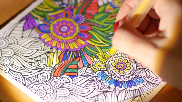Painting adult coloring book at evening home by reading-lamp light