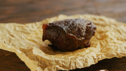Closeup shot of small piece of delicious fried meat lying on parchment paper on wooden tabletop
