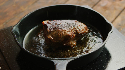 Metal frying pan with piece of delicious roasted meat standing on modern stove on wooden tabletop