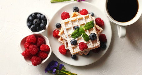 From above shot of cup of aromatic coffee and bowls with fresh berries standing near plate with delicious soft waffles