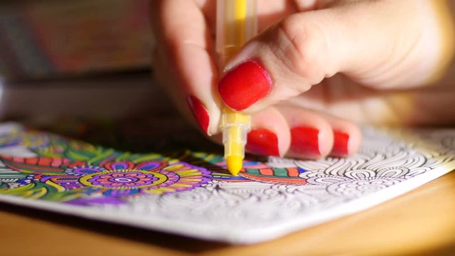 Painting adult coloring book at evening home by reading-lamp light