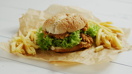 Closeup shot of yummy French fries and tasty chicken burger lying on parchment paper on white timber tabletop