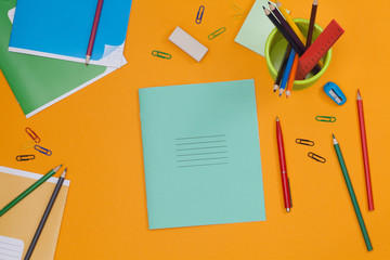 School notebook for your text over colorful supplies on orange background. Back to school concept with copy space. Flat lay. Top view.