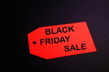 Black friday sale concept. Fourth Friday of November, beginning of Christmas shopping season since 1952. Red tag with black text on bright red background. Copy space, close up, top view, flat lay.