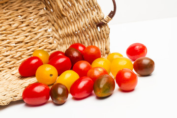 Tomates cherry en cesta de mimbre y fondo blanco aislado. Vista de frente