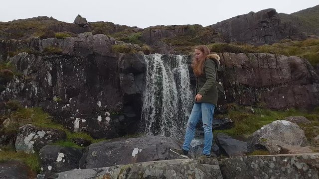Pretty girl walks along a waterfall in the nature of Ireland