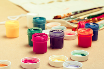 Jars with colorful gouache and brush on beige background close up