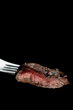 Piece of a grilled medium rare steak on a fork. Vertical image with copy space. Isolated on black.