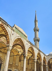 Principal entry to the Arcaded courtyard of The Sultan Ahmet Camii Mosque, also known as The Blue Mosque, with a minaret in the background. Istanbul, Turkey.