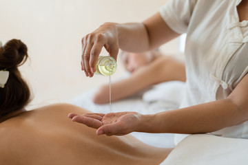 Masseuse pour oil on the hand and young asian woman relaxing receiving back massage at spa salon