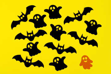 Holiday decorations for Halloween. Black paper bats and ghosts and orange paper ghost on a yellow background, top view.