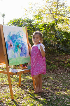A pre-school girl painting at an easel in a garden. 