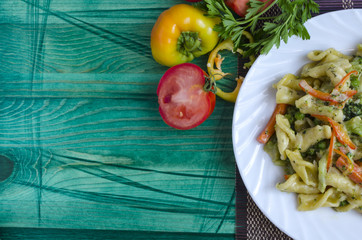 Pasta with vegetables and cheese in a white plate on a green background copy space