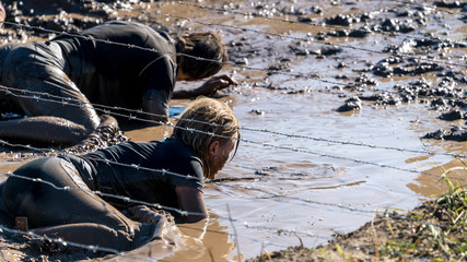 Sexy female athlete crawling under barbed wire at an obstacle course race 