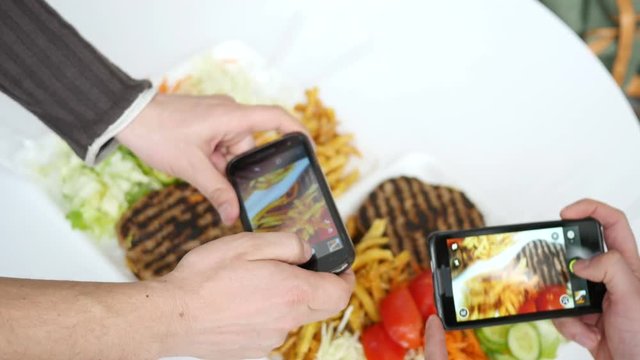Friends take a photo picture of food via two smartphone above a dish