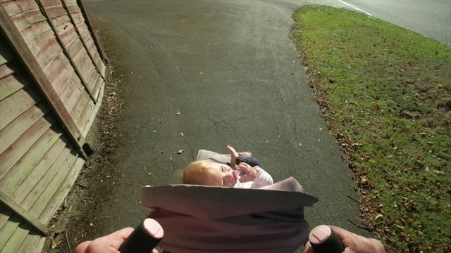 Slow motion personal perspective of a Caucasian man pushing his daughter in a a stroller along a street themes of fatherhood babysitting child pram