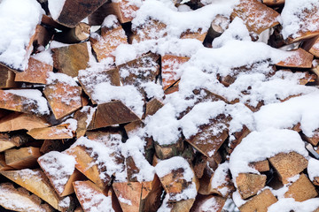 Winter background texture pattern with stacked dry chopped firewood logs covered with snow