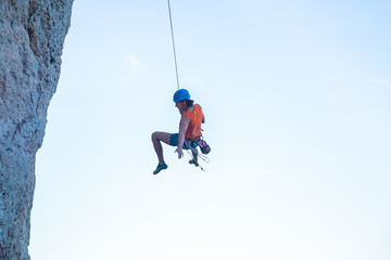 View of man in hardhat hanging on rope while doing rappel and showing pirouettes flying in air 