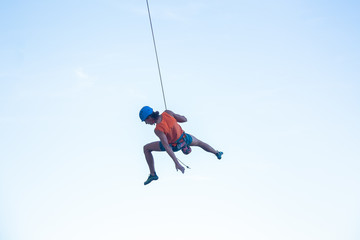 View of man in hardhat hanging on rope while doing rappel and showing pirouettes flying in air 